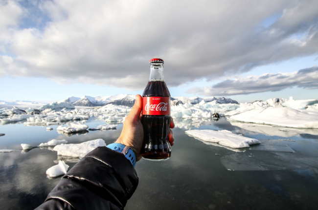Glass bottle of coca cola being held in front of icebergs
