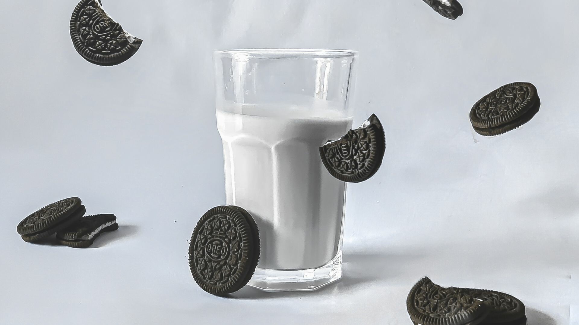 Cup of milk with oreos falling around it.