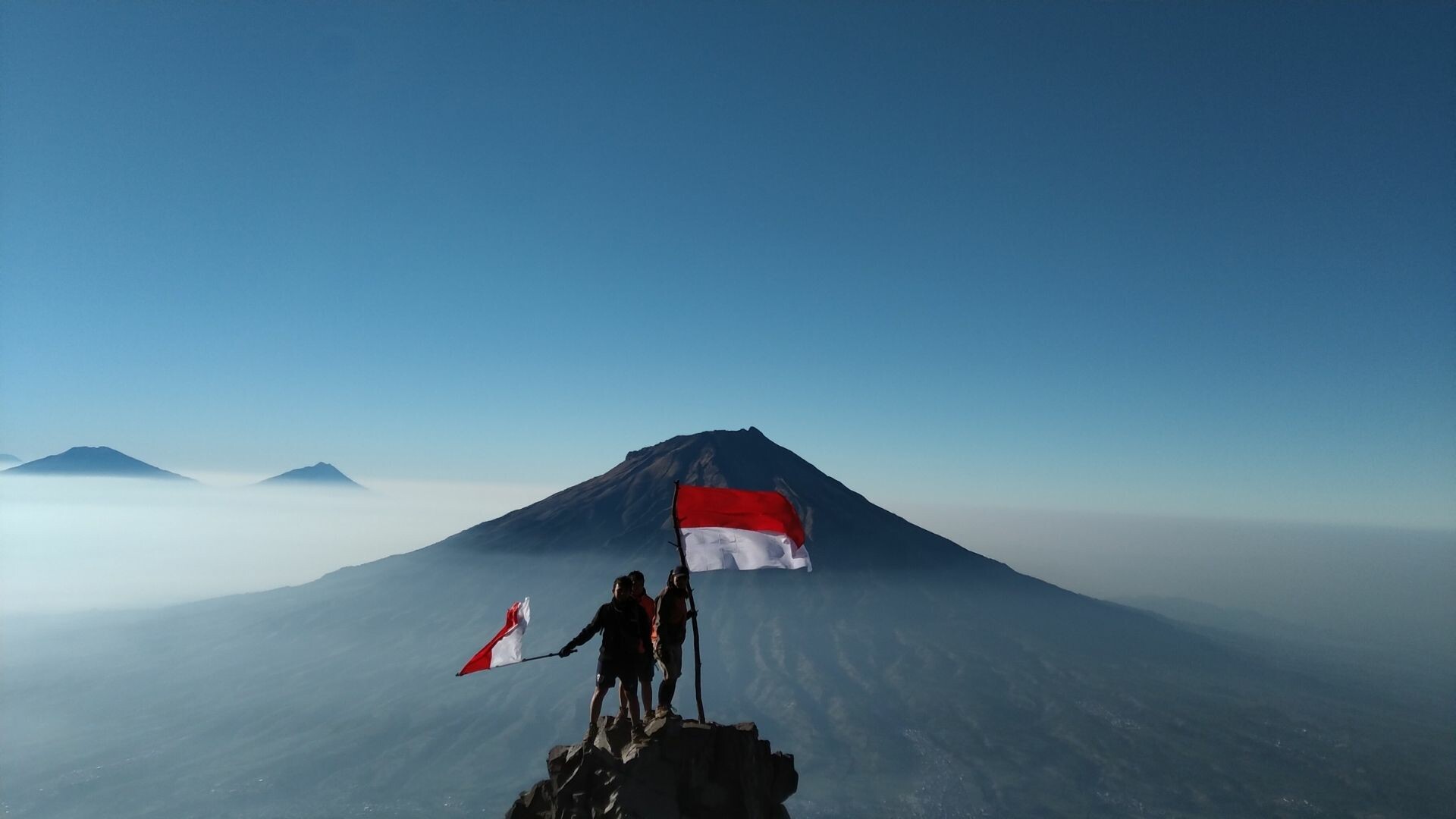 People standing on top of a mountain with Indonesian flag.