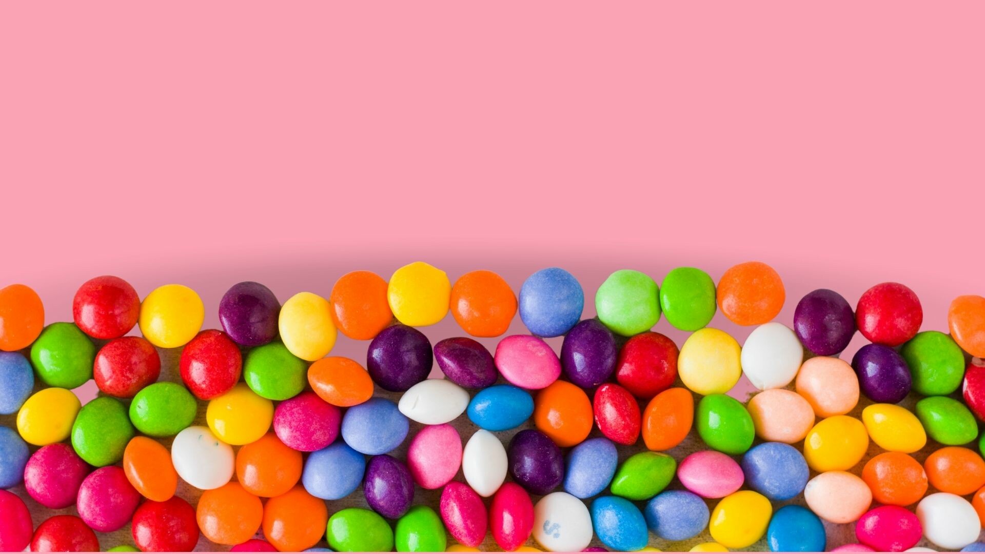 Skittles on a pink background.