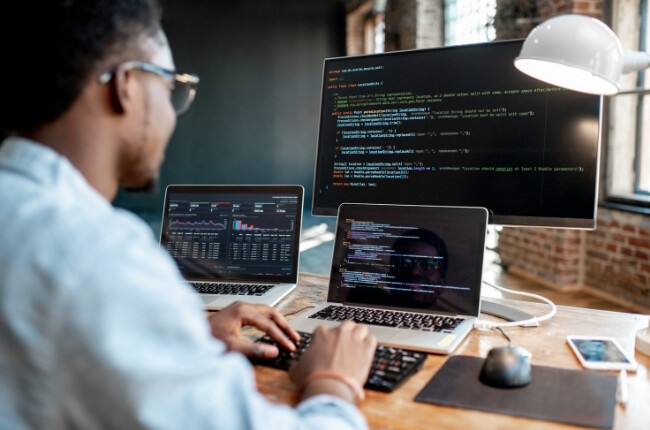 man coding on three screens