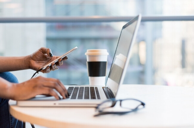 woman typing on a laptop and looking at her phone