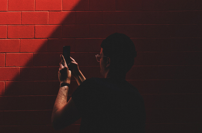 Person taking photo on phone against red brick wall